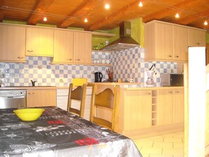 A kitchen with wooden cabinets, a checkered backsplash, a yellow bowl, and a table with a tablecloth. - Apartment in house in the massif de l'épine near lac d'Aiguebelette (Marcieux)