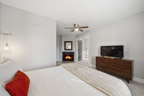 A bedroom with a bed, a television, a dresser, a ceiling fan, and a fireplace.