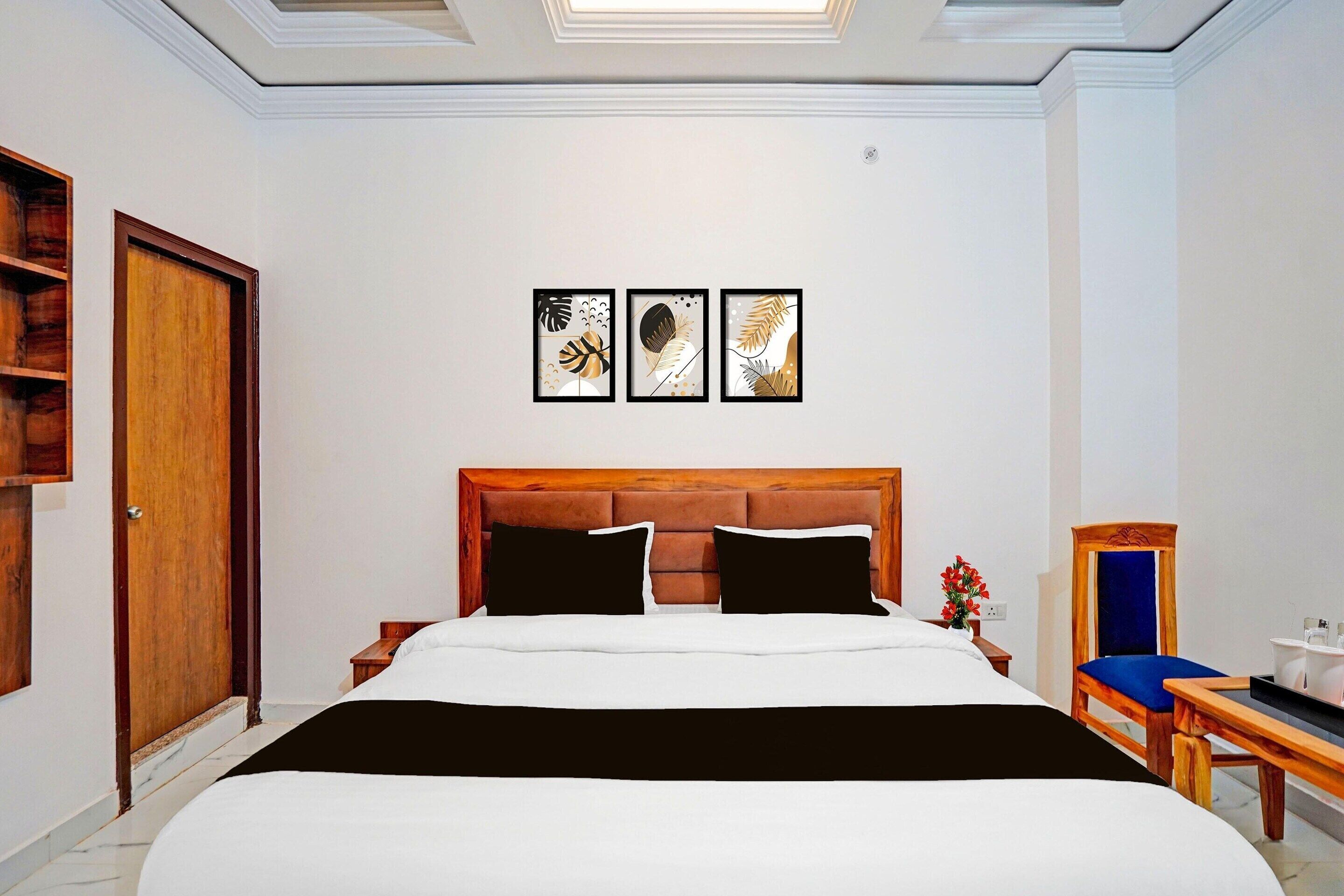 Hotelkamer met een groot bed, een houten hoofdbord, een nachtkastje met een lamp, een stoel en drie ingekaderde kunstwerken aan de muur.