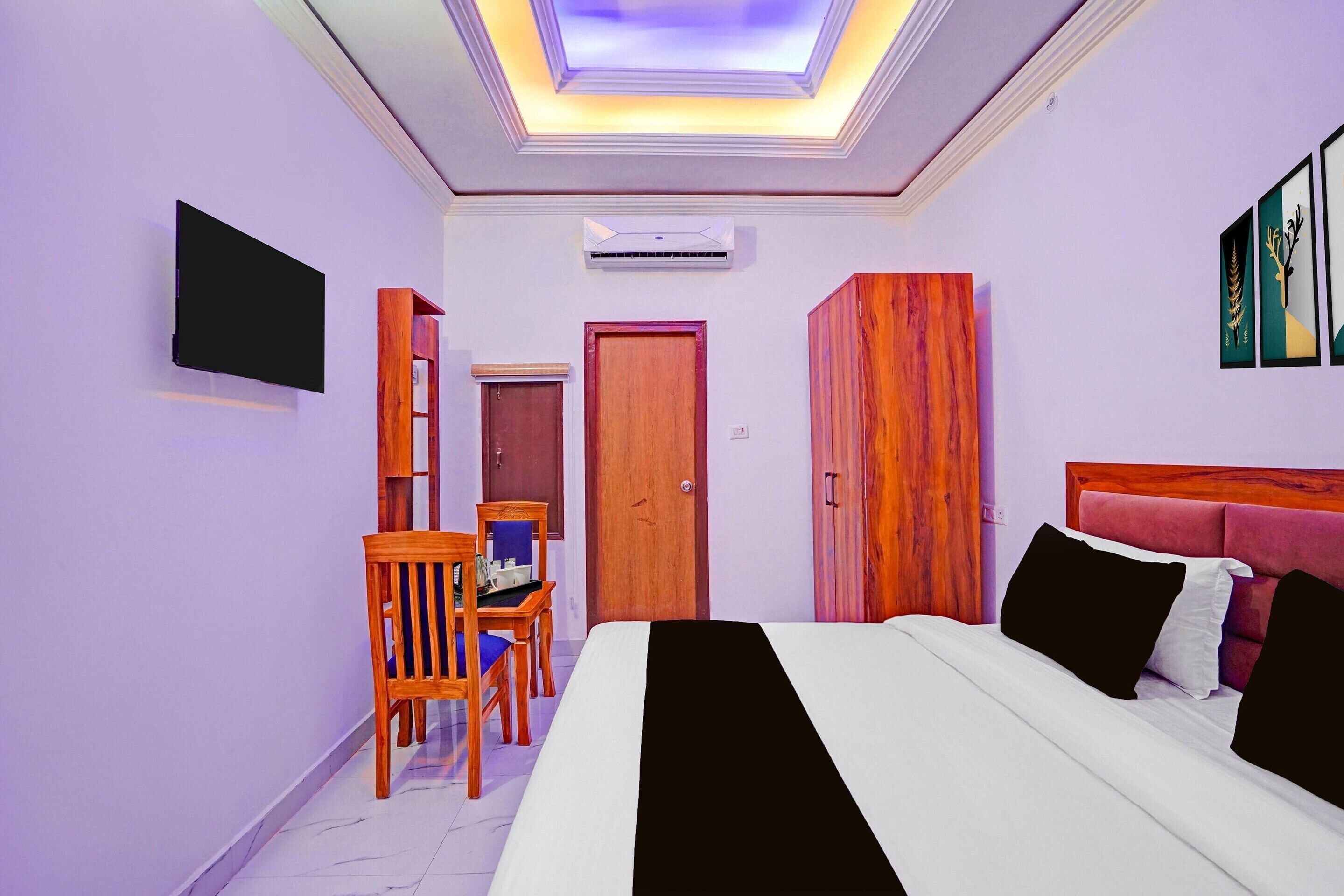 A hotel room with a bed, a desk with a chair, a wardrobe, a television, and a door.