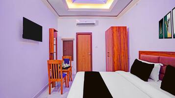 A hotel room with a bed, a desk with a chair, a wardrobe, a television, and a door.