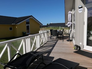 A wooden deck with outdoor furniture, a white railing, and a building with the number 123. - 4 Star Holiday Home in Grossenbrode (Grossenbrode)