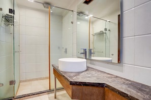 Een moderne badkamer met een douchecabine van glas, een marmeren aanrechtblad en een grote spiegel.