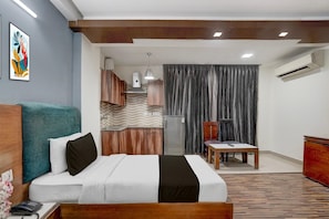 Hotelkamer met een bed, bureau, stoel, klein tafeltje, airconditioning, koelkast, wandtelefoon en decoratief muurdecoratie.