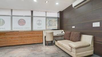 A room with a desk, a chair, a sofa, and a wall-mounted air conditioner.