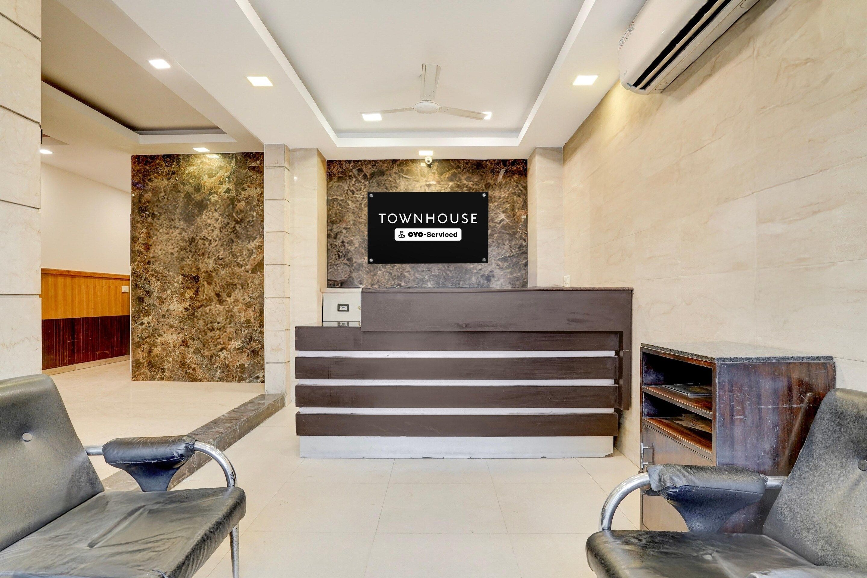 A reception area with a marble wall, a sign indicating it's serviced by OYO, and two black leather chairs.