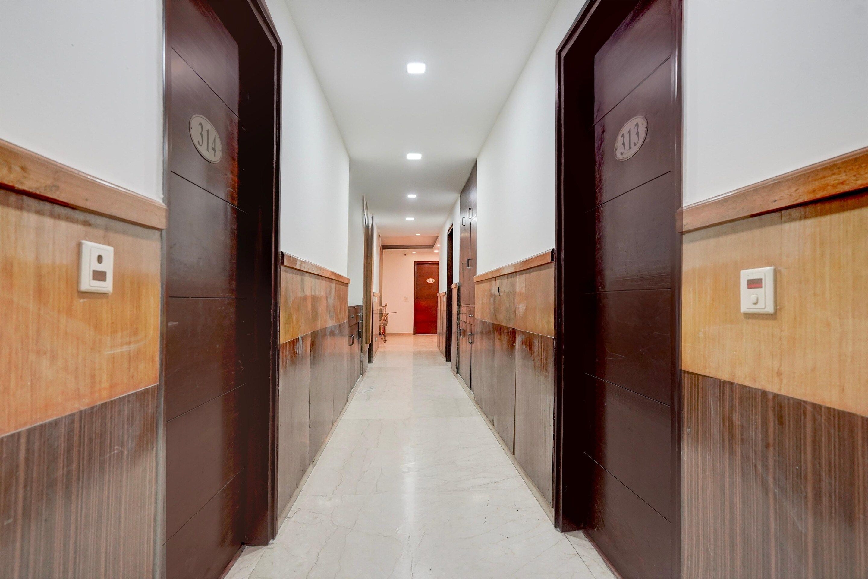A hallway with wooden paneling and numbered doors, leading to a room with a red door at the end.
