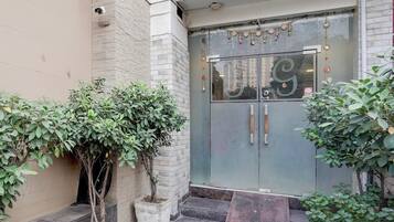Entrada de un edificio con puerta de cristal, cámara de seguridad y plantas en macetas.