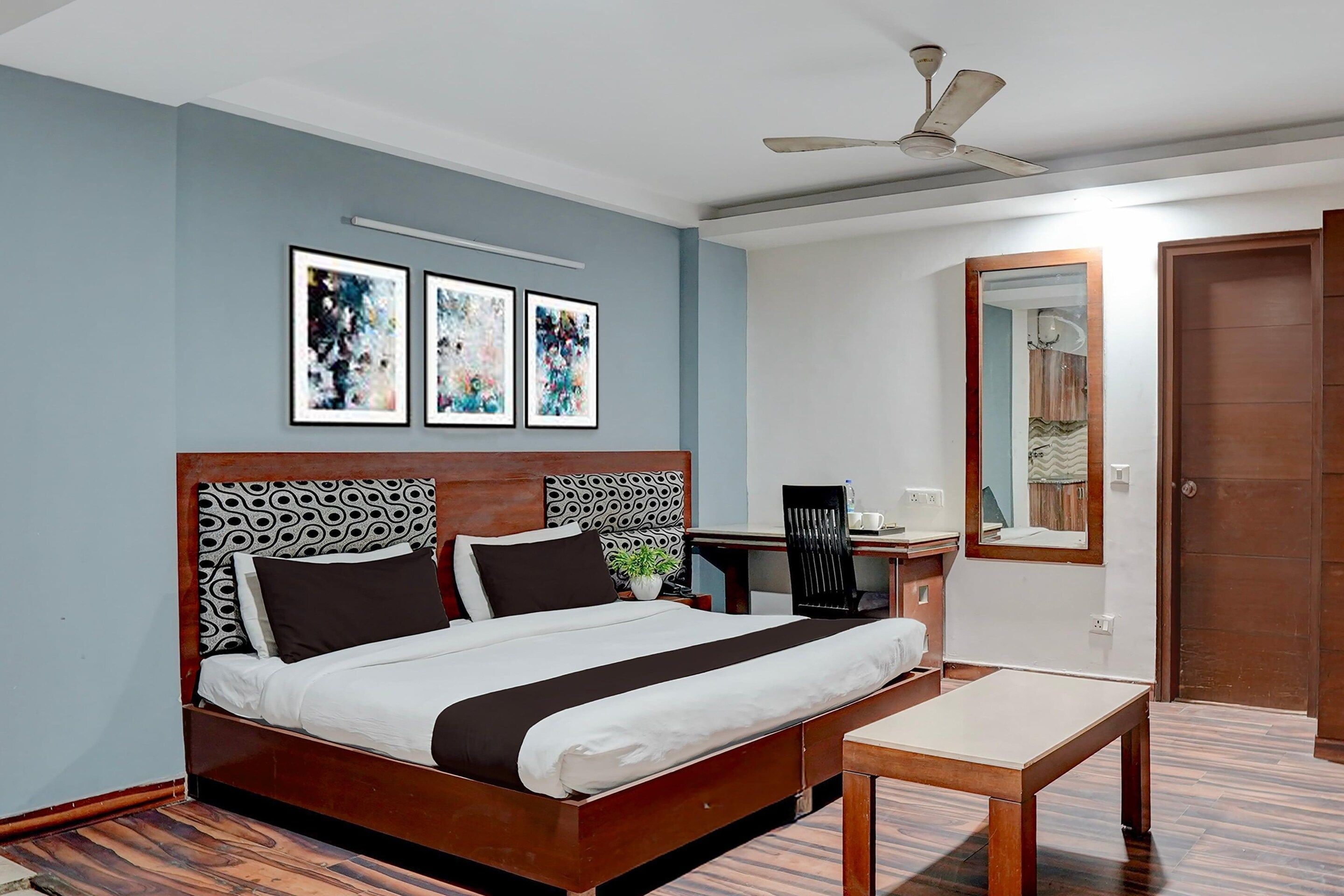 Habitación de hotel con cama, escritorio, silla, ventilador de techo y tres obras de arte enmarcadas en la pared.