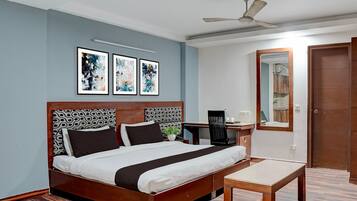 Habitación de hotel con cama, escritorio, silla, ventilador de techo y tres obras de arte enmarcadas en la pared.