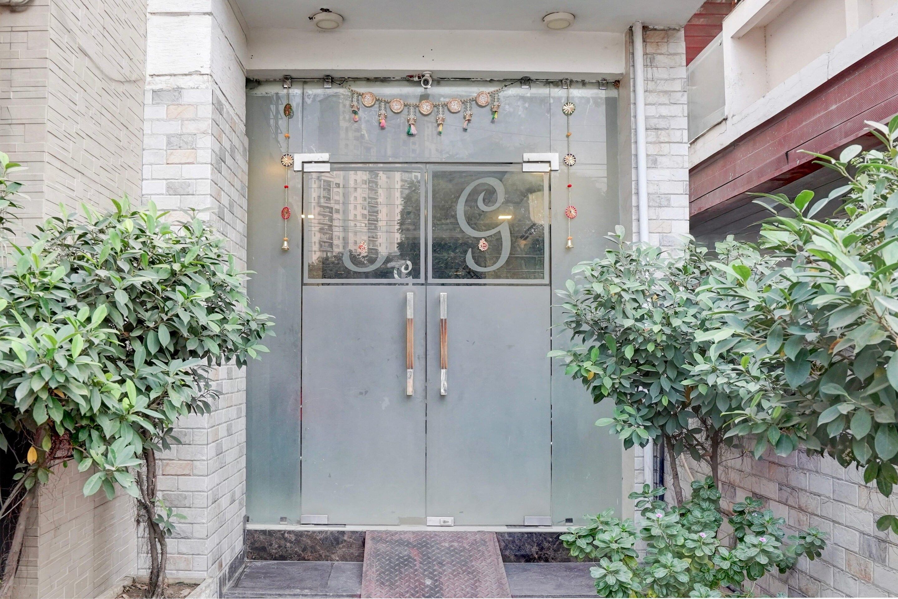 Une entrée moderne, avec une grande porte en verre ornée d’une lettre « G » décorative.