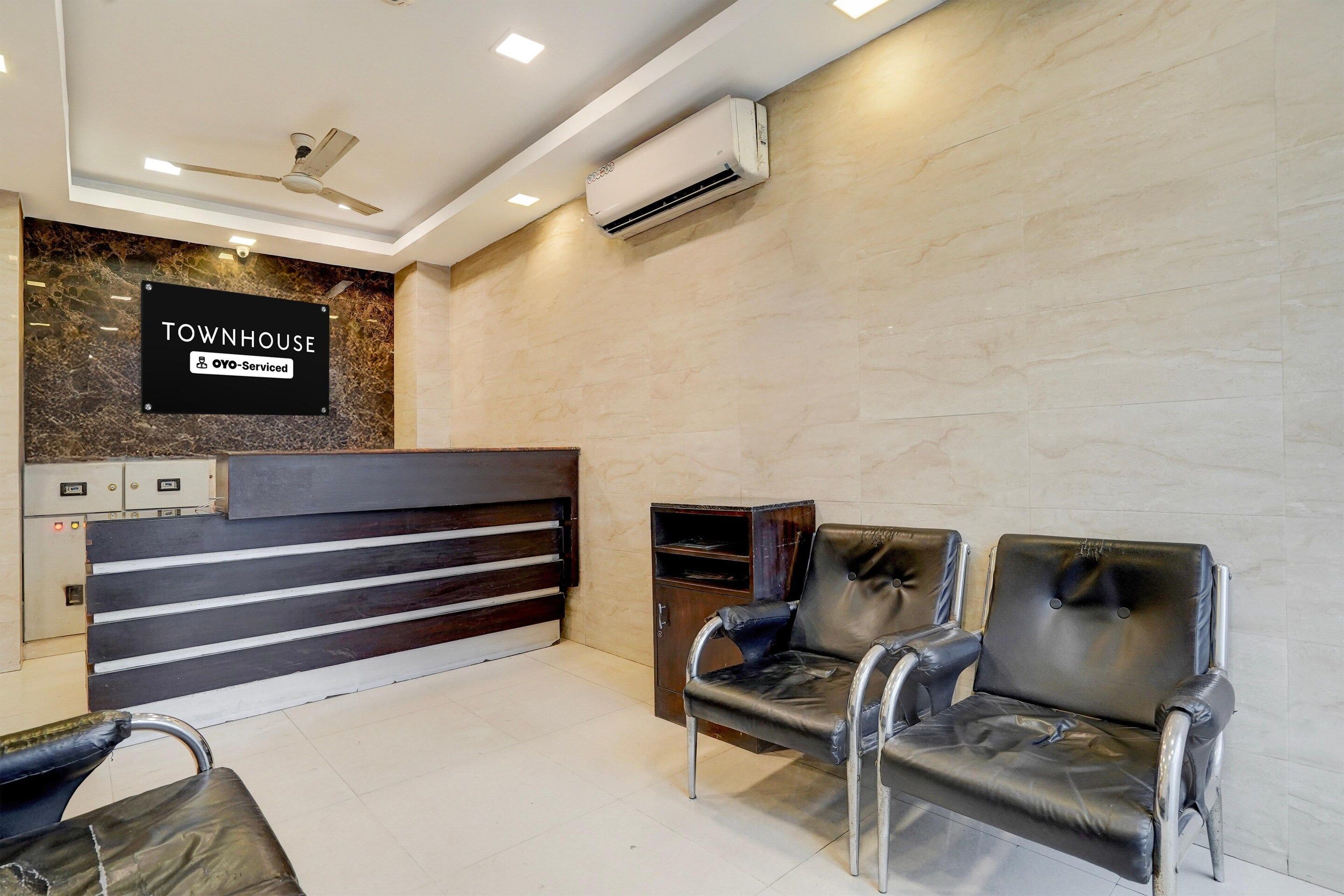 Un área de recepción con un cartel que indica que es un espacio de autoservicio, una mesa de recepción, dos sillones de cuero y un equipo de aire acondicionado.