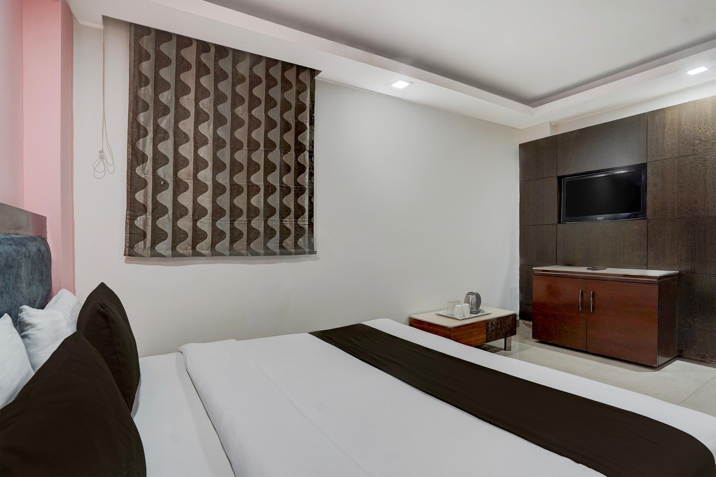Un dormitorio con cama, televisor montado en un mueble y cortina estampada.