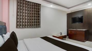 Un dormitorio con cama, televisor montado en un mueble y cortina estampada.