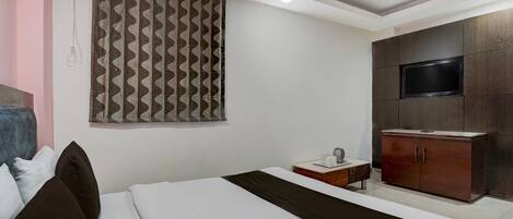 Un dormitorio con cama, televisor montado en un mueble y cortina estampada.