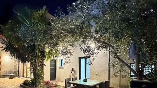Eine Terrasse im Freien mit Steinboden, einem Tisch mit Stühlen und einer kleinen Gartenanlage mit Pflanzen und einer Bank.