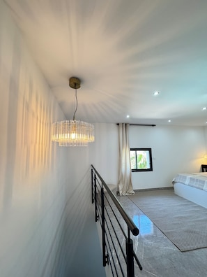 Ein modernes Schlafzimmer mit einem großen Bett, einer Pendelleuchte, einem Fenster mit Vorhängen und einer Treppe mit Geländer.