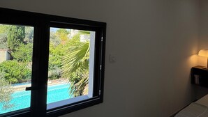 Ein Zimmer mit Fensterblick auf einen Swimmingpool, einer Deckenleuchte und einem Nachttisch mit Lampe.