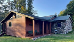En stuga byggd av trä med en veranda, en stenmur och en liten trädgårdsyta.