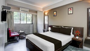 Une chambre d’hôtel avec un grand lit, une chaise, une petite table avec une lampe, un appareil de climatisation et une fenêtre avec des rideaux.