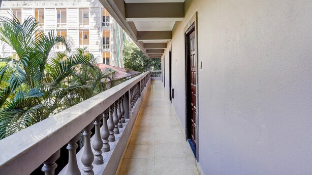 Un pasillo con barandilla, suelo de baldosas y vistas a un edificio con ventanas y vegetación.