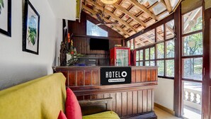 Zona de recepción de un hotel con mostrador de madera, un letrero que dice 'HOTELO' y un amplio ventanal con vistas al exterior.
