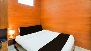 A hotel room with a wooden paneled wall, a bed with white and black bedding, a bedside lamp, and a window. - Deluxe Collection O Kalyan Nagar Bangalore (Bengaluru)