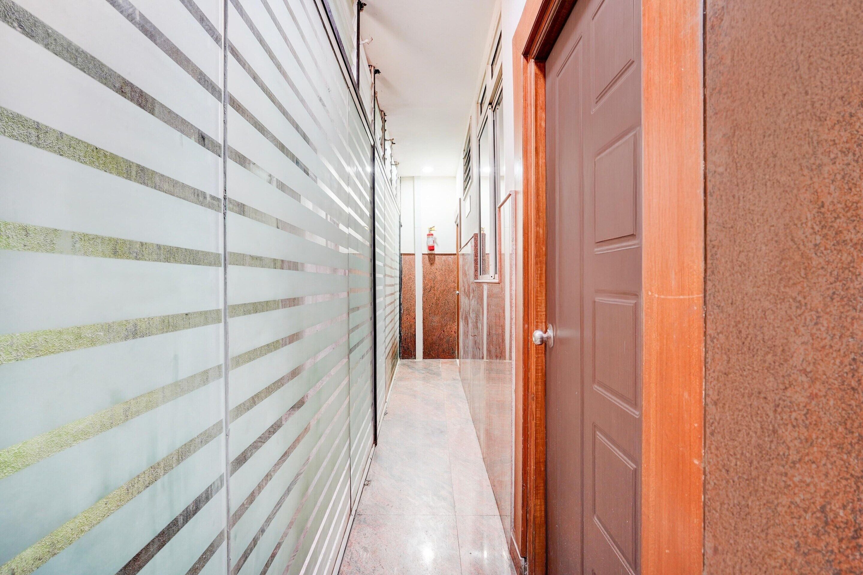 Un pasillo con un muro de cristal, una puerta de madera y un extintor.