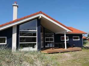Ein modernes Haus mit rotem Dach, großen Fenstern und einer Holzterrasse.