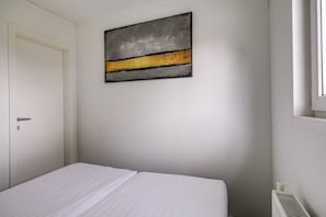 Een slaapkamer met een bed, een deur, een radiator en een kunstwerk aan de muur.