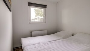 Pieni huone, jossa on yksi sänky, ikkuna, valkoiset seinät ja patteri.