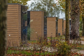 A row of wooden cabins with a natural setting, including trees and foliage. - Cube 16 | stijlvol en licht 4 persoons chalet (Zennewijnen)