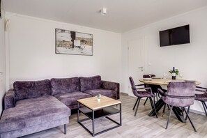 Ein modernes Wohnzimmer mit einem grauen Sofa, einem Holztisch und einem Essbereich mit violetten Stühlen.