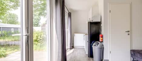Un pasillo con puerta corredera de vidrio, un refrigerador blanco, un basurero y un banco.