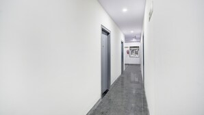 Un couloir aux murs blancs, au sol gris, et une porte au fond.