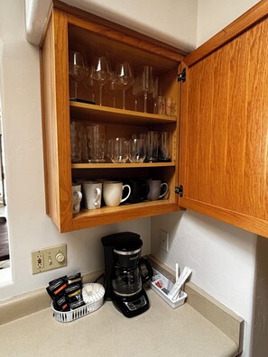 A kitchen with a wooden cabinet containing glassware and mugs, a coffee maker, and coffee pods on the counter. -  Saguaro West Retreat, Fire Pit, Desert Views & Peaceful Stay! Animal friendly (Tucson)