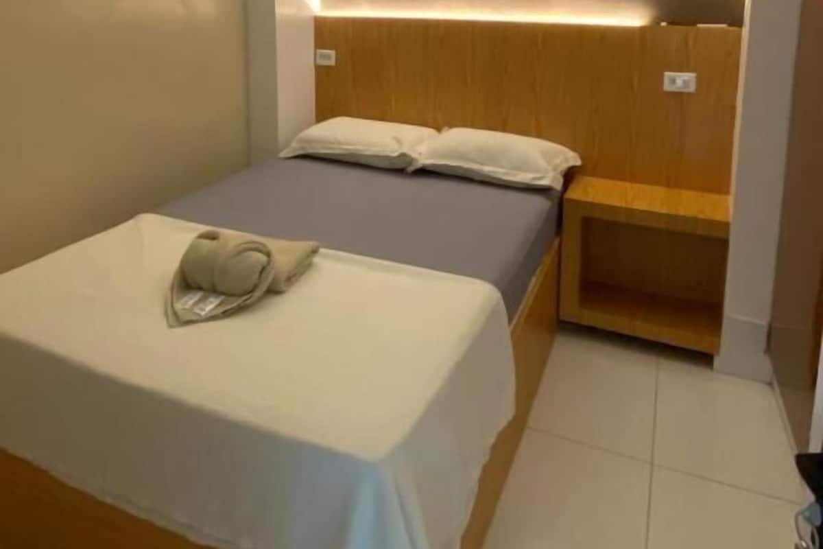 Un lit simple avec une tête de lit, une table de chevet et un luminaire fixé au mur.