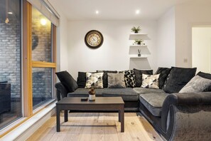 Un salon moderne avec un canapé gris, une table basse foncée et une horloge murale.
