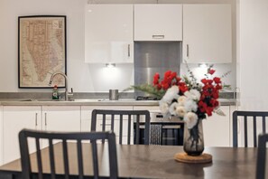 Une cuisine moderne avec des armoires blanches, une hotte en acier inoxydable et un coin repas comprenant une table et des chaises.