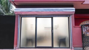 Ein Gebäudeeingang mit Glastür, Metallgitter und roter Wand.