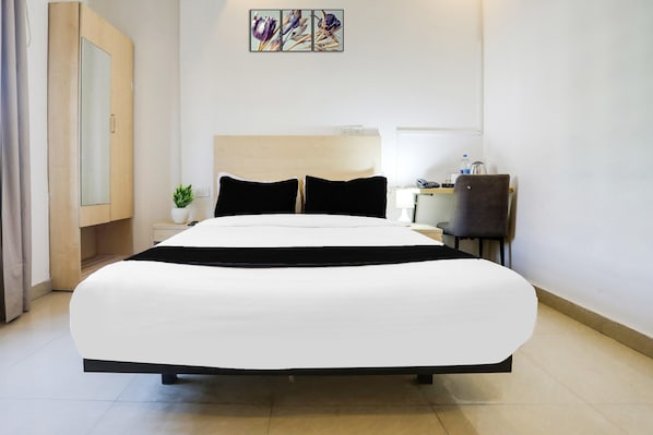 Habitación de hotel con una cama grande, un escritorio, una silla, una planta en maceta y una obra de arte colgada en la pared.