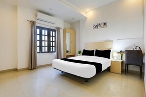 A hotel room with a bed, a desk, a chair, a nightstand, a lamp, a mirror, and a window with curtains.
