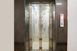 An elevator with a glass door, a control panel with a red light, and a metallic wall.