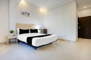 A modern hotel room with a large bed, a bedside table with a lamp, a small plant, and a wall-mounted artwork.