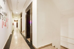 Un largo y estrecho pasillo de hotel con piso pulido, un extintor y una puerta al final.
