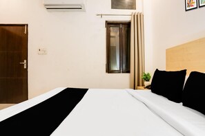 A hotel room with a bed, a window with curtains, a wall-mounted air conditioner, and a door.