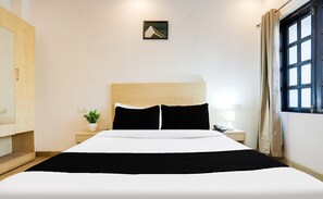 A hotel room with a bed, a nightstand with a lamp, a small potted plant, and a window with curtains.
