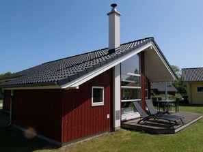 A red building with a sloped roof and a chimney, a glass door entrance, and a patio with outdoor furniture. - 4 Star Holiday Home in Grossenbrode (Grossenbrode)