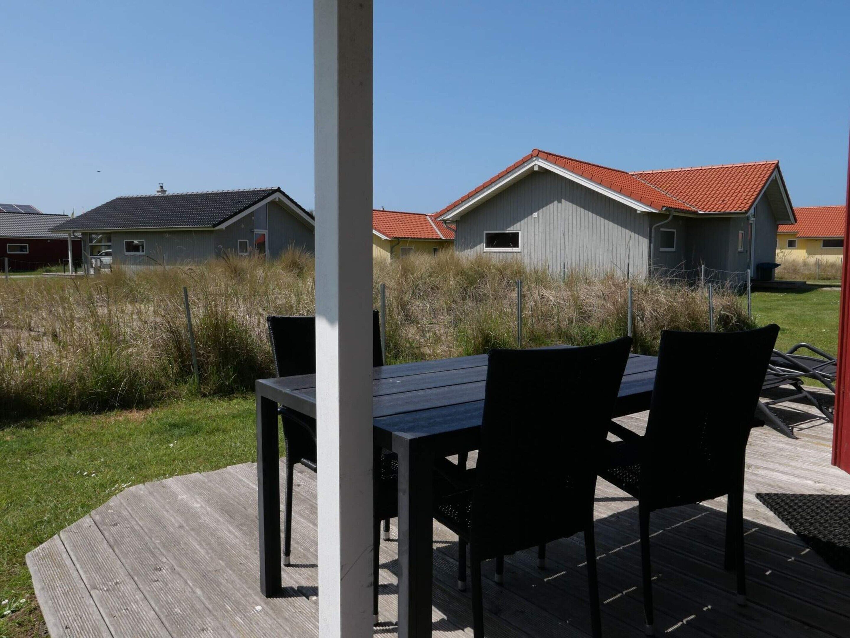 A wooden deck with a table and chairs, overlooking a grassy area with houses in the background.