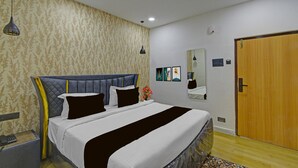A bedroom with a bed, a bedside table, a telephone, a mirror, and a door.